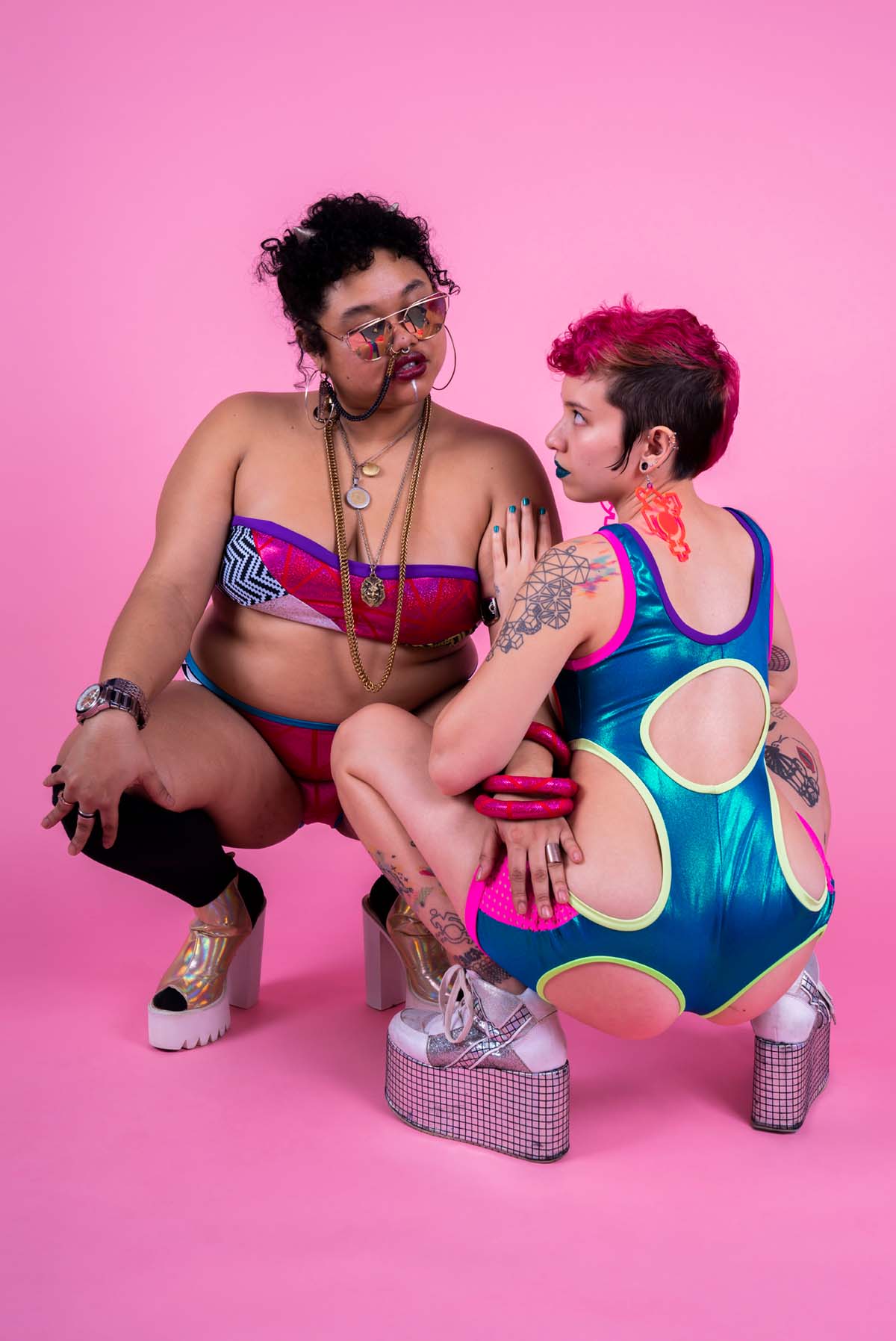 Two people posing in front of a pink backdrop wearing colorful spandex clothing by Rebirth Garments