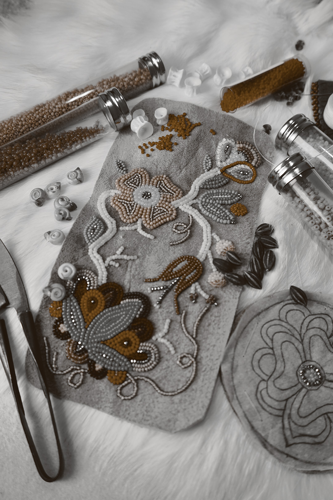 Sepia image of tubes of beads and floral beadwork on suede